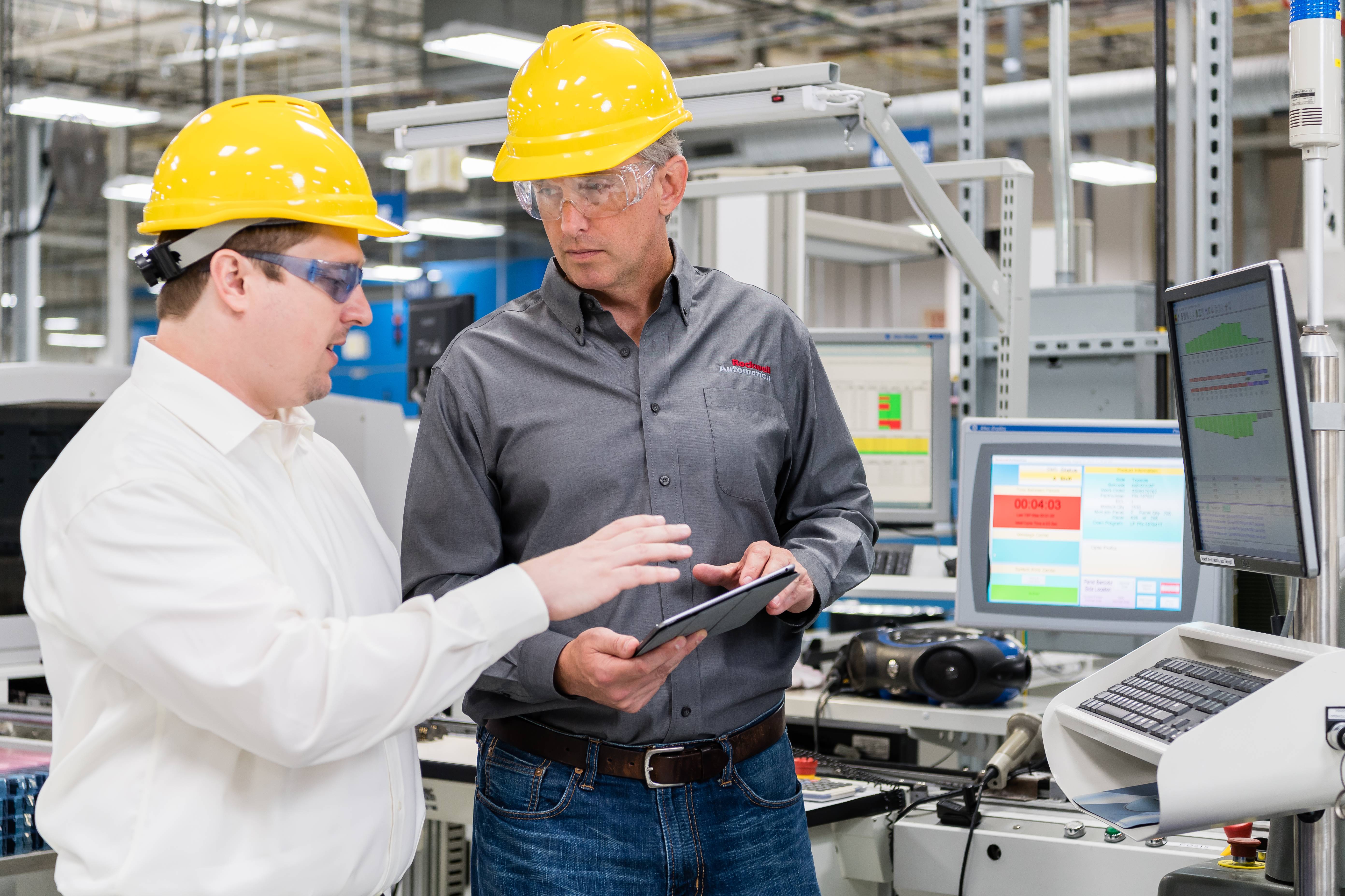 two men wearing hard hats looking at a tablet